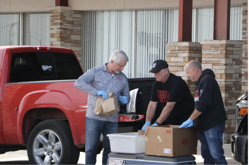 men wearing glove pass out sack lunches in a drive through during the pandemic