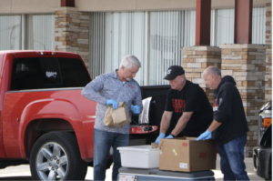 men wearing glove pass out sack lunches in a drive through during the pandemic