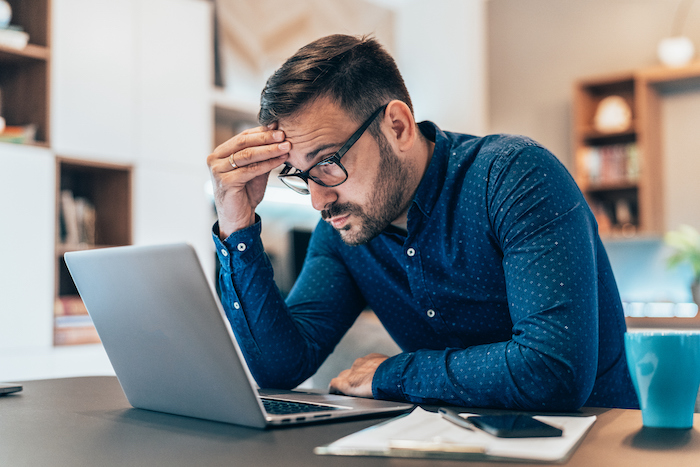 Tired young businessman working at home using lap top and looking Anxious