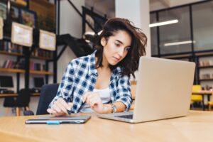 Smart pretty young woman working with laptop on table in library. Studying in university, learning,