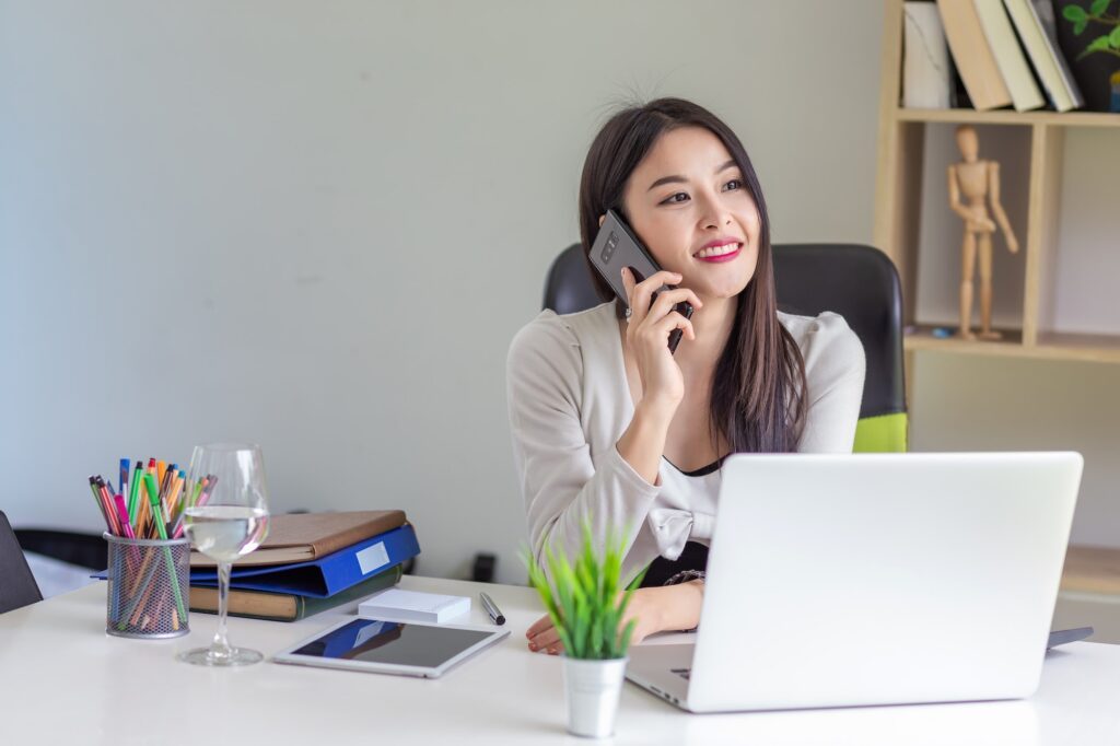 Happy beautiful Asian businesswoman talking on the phone the laptop is placed on the office desk. Brand Image, Press Releases, Public Relations, Corporate Reputation, Brand Awareness, Customer Perception