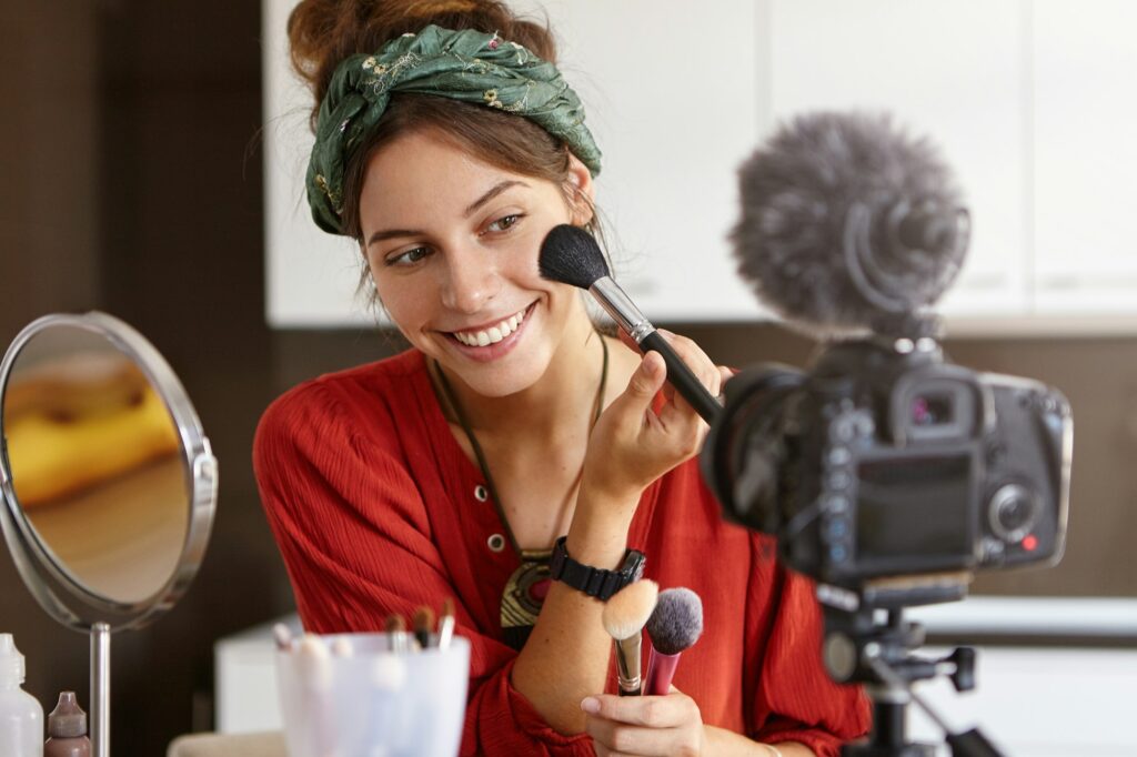 Portrait of beautiful smiling female vlogger makes video review, uses cosmetic product, records use brand loyalty